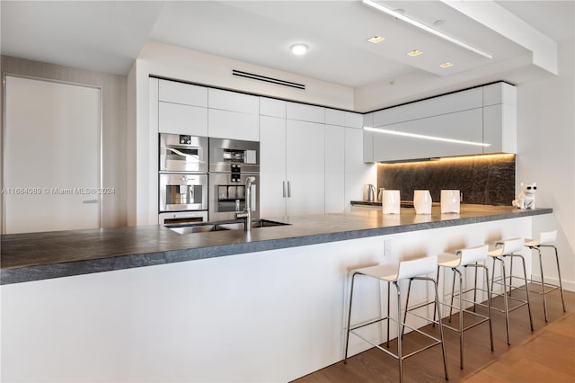 7065 Fisher Island Dr Unit 7065, Miami Beach, FL 33109 - kitchen featuring dark countertops, a sink, a peninsula, wood finished floors, and a kitchen bar