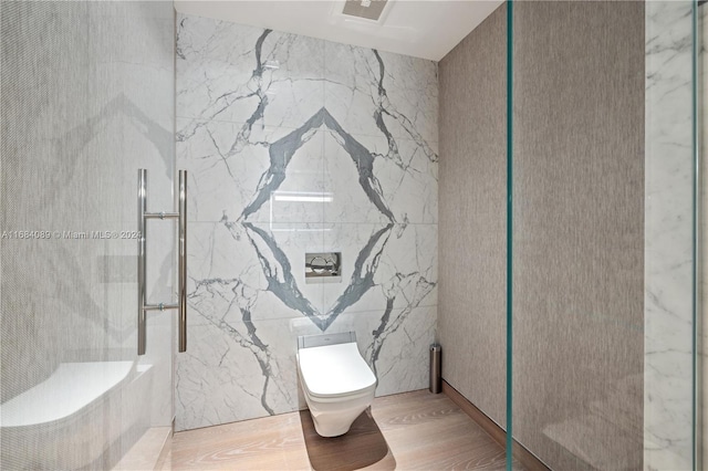 bathroom featuring hardwood / wood-style flooring, toilet, a tile shower, and tile walls