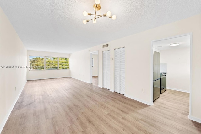 spare room featuring light hardwood / wood-style floors, a textured ceiling, and an inviting chandelier