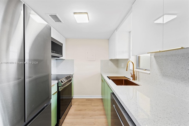 kitchen with light stone counters, white cabinets, sink, light wood-type flooring, and appliances with stainless steel finishes