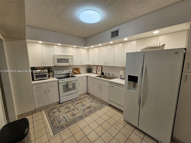 kitchen with white cabinetry, a textured ceiling, light tile patterned floors, sink, and white appliances