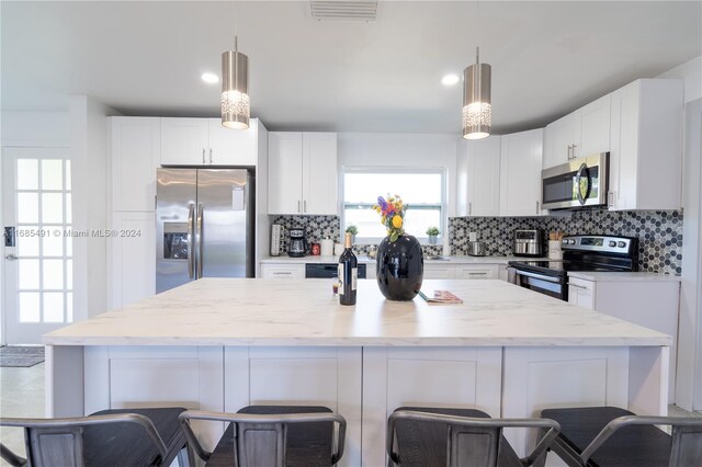 kitchen featuring stainless steel appliances, white cabinetry, tasteful backsplash, and a center island