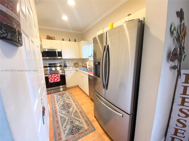 kitchen with light tile patterned flooring, ornamental molding, stainless steel appliances, white cabinetry, and sink