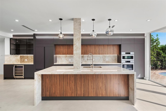 kitchen featuring light stone counters, wine cooler, backsplash, pendant lighting, and sink