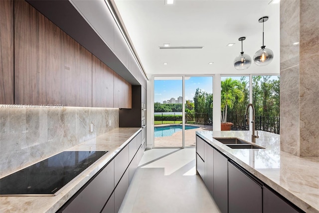 kitchen with black electric cooktop, light stone counters, sink, backsplash, and decorative light fixtures