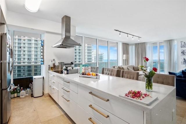 kitchen featuring stainless steel fridge, white cabinetry, plenty of natural light, and wall chimney exhaust hood