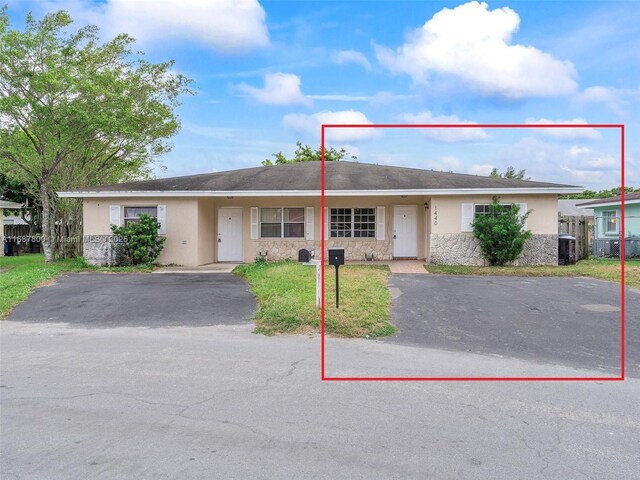 view of front of property featuring central AC, aphalt driveway, a front lawn, stone siding, and stucco siding
