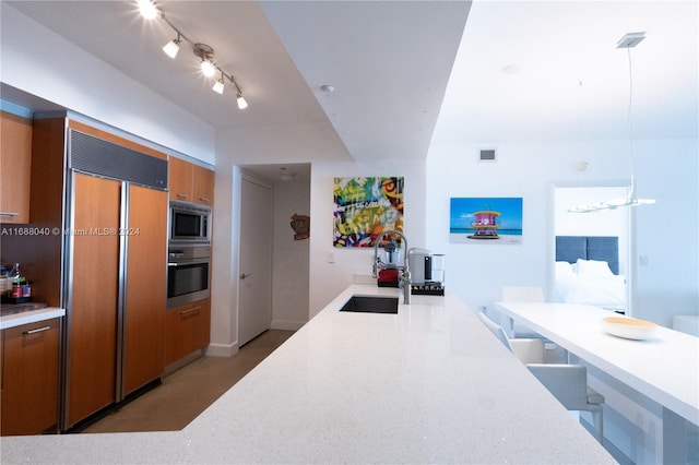 kitchen featuring built in appliances, sink, and pendant lighting