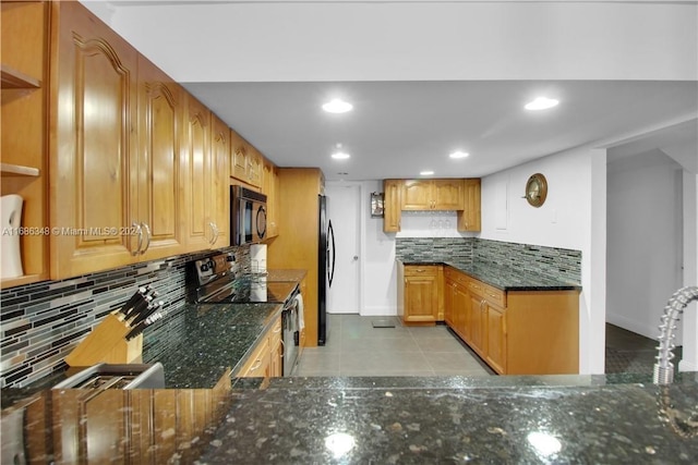 kitchen with black appliances, kitchen peninsula, dark stone counters, light tile patterned floors, and decorative backsplash