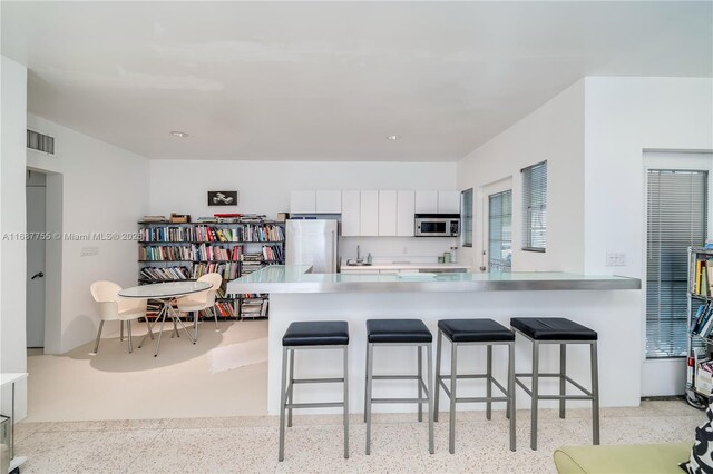 kitchen featuring kitchen peninsula, appliances with stainless steel finishes, a kitchen bar, and white cabinets