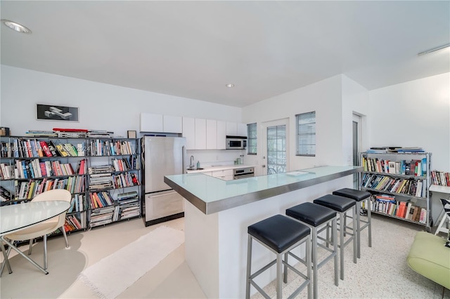 kitchen with a kitchen bar, stainless steel appliances, white cabinets, kitchen peninsula, and sink