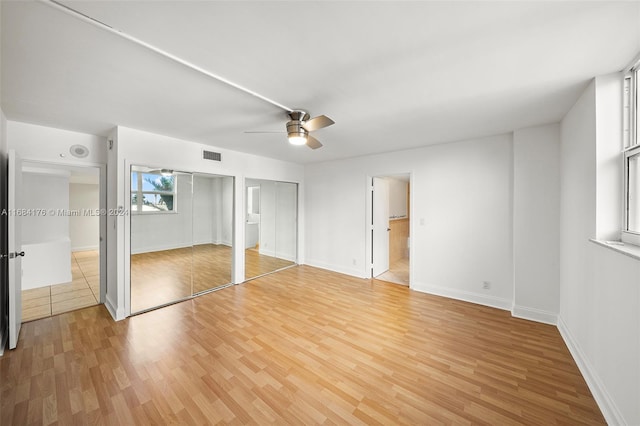 unfurnished bedroom featuring multiple closets, light hardwood / wood-style floors, and ceiling fan