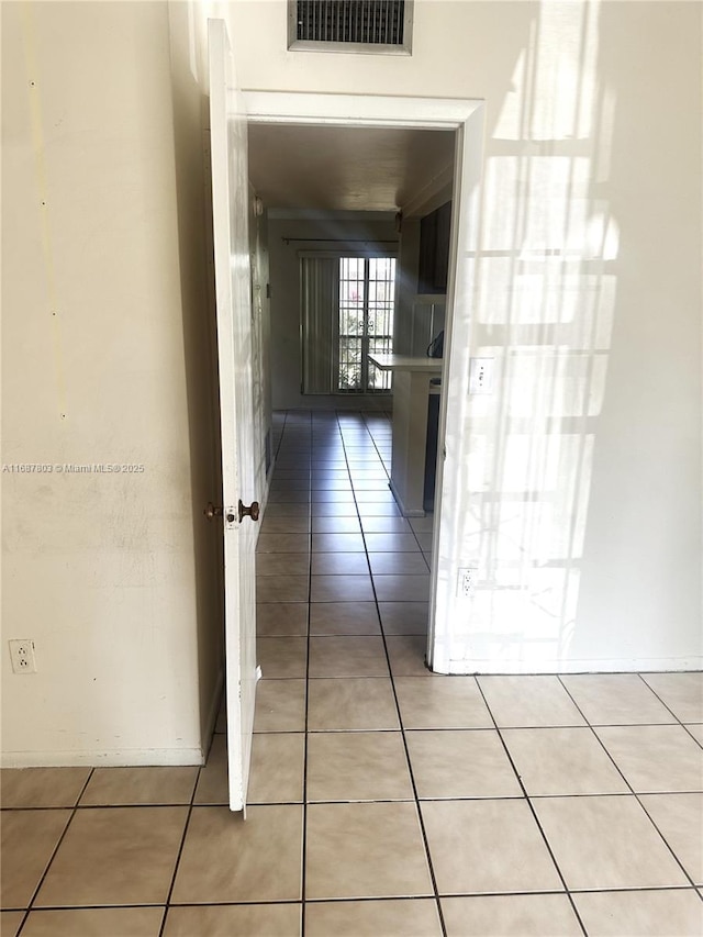 corridor with baseboards, visible vents, and light tile patterned flooring