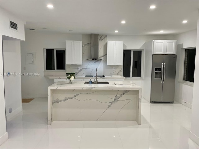 kitchen with white cabinets, a kitchen island with sink, wall chimney range hood, light stone countertops, and stainless steel fridge