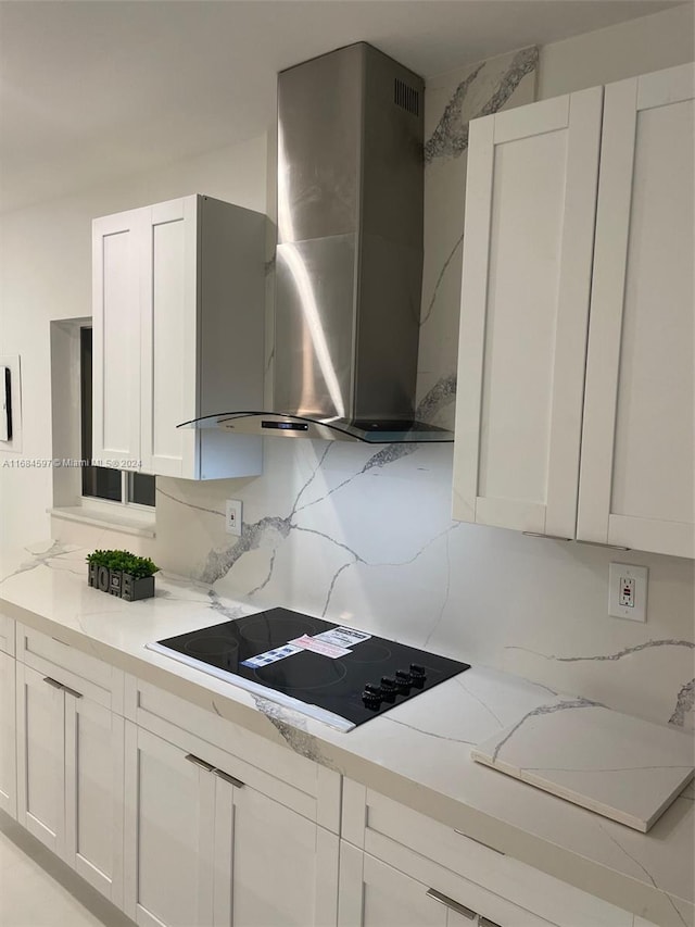 kitchen featuring light stone counters, backsplash, white cabinetry, black electric cooktop, and wall chimney exhaust hood