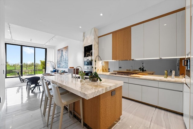 2811 S Bayshore Dr Unit 4C, Miami, FL 33133 - kitchen featuring white cabinets, a center island with sink, a breakfast bar area, light stone counters, and stainless steel gas stovetop