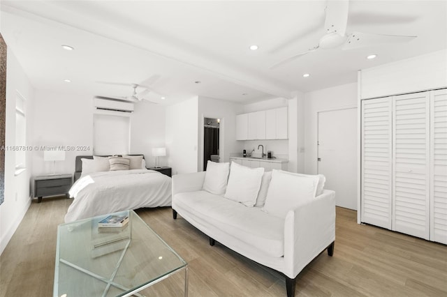 bedroom with light hardwood / wood-style floors, ceiling fan, sink, and a wall mounted AC