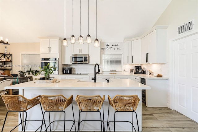 kitchen with a center island with sink, sink, appliances with stainless steel finishes, hanging light fixtures, and white cabinets