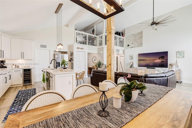 dining room with beam ceiling, high vaulted ceiling, sink, light hardwood / wood-style floors, and beverage cooler