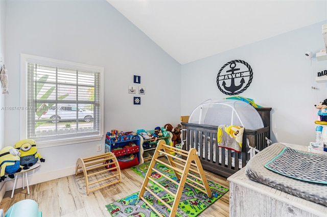 bedroom with high vaulted ceiling, a nursery area, and hardwood / wood-style flooring