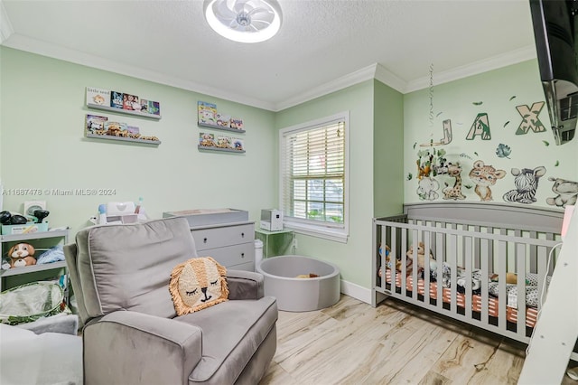 bedroom with ornamental molding, a nursery area, a textured ceiling, and light hardwood / wood-style flooring