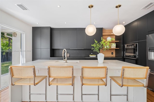 kitchen with a breakfast bar area, sink, a large island, pendant lighting, and light hardwood / wood-style flooring