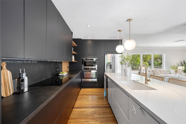 kitchen with light hardwood / wood-style flooring, hanging light fixtures, sink, tasteful backsplash, and appliances with stainless steel finishes