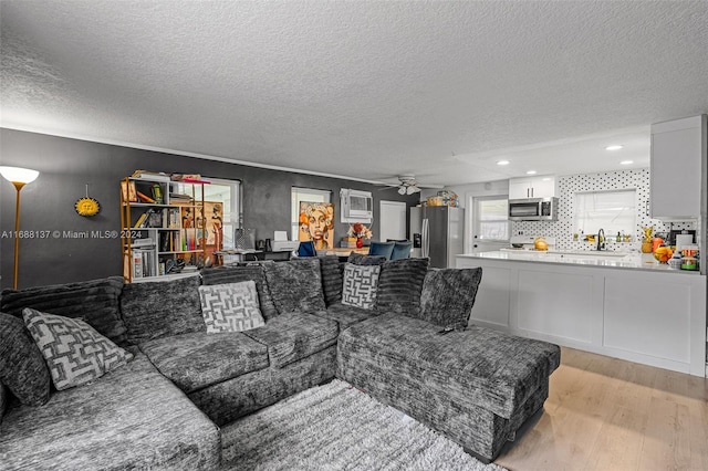 living room featuring a textured ceiling, ceiling fan, and light hardwood / wood-style flooring