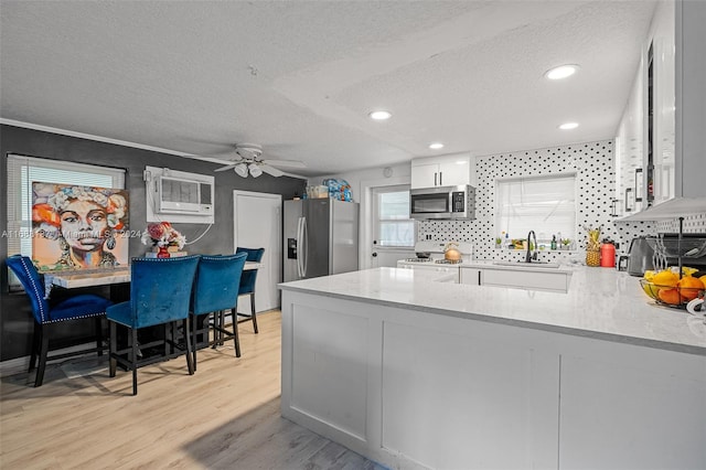 kitchen featuring kitchen peninsula, appliances with stainless steel finishes, a textured ceiling, white cabinets, and light wood-type flooring