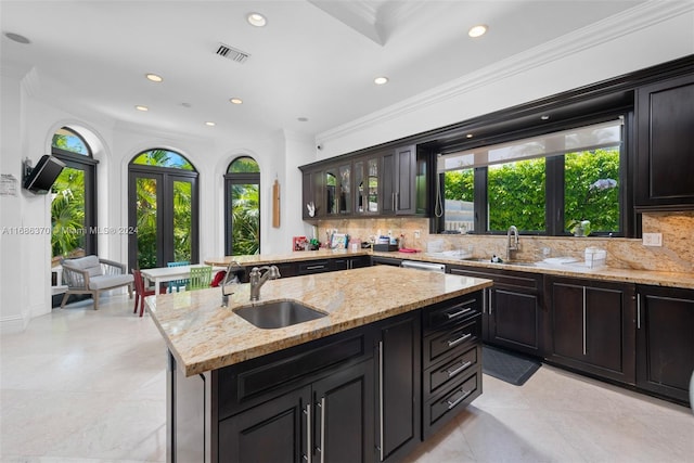 kitchen featuring sink, ornamental molding, tasteful backsplash, light stone countertops, and a kitchen island with sink