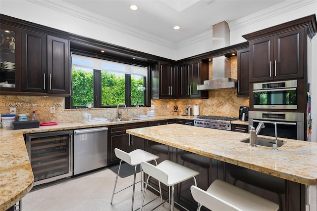 kitchen with ornamental molding, stainless steel appliances, wine cooler, dark brown cabinets, and wall chimney exhaust hood