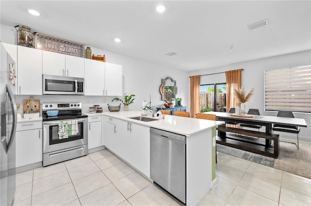 kitchen with white cabinets, sink, light tile patterned floors, kitchen peninsula, and stainless steel appliances