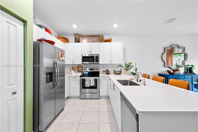 kitchen with white cabinetry, sink, kitchen peninsula, light tile patterned floors, and appliances with stainless steel finishes