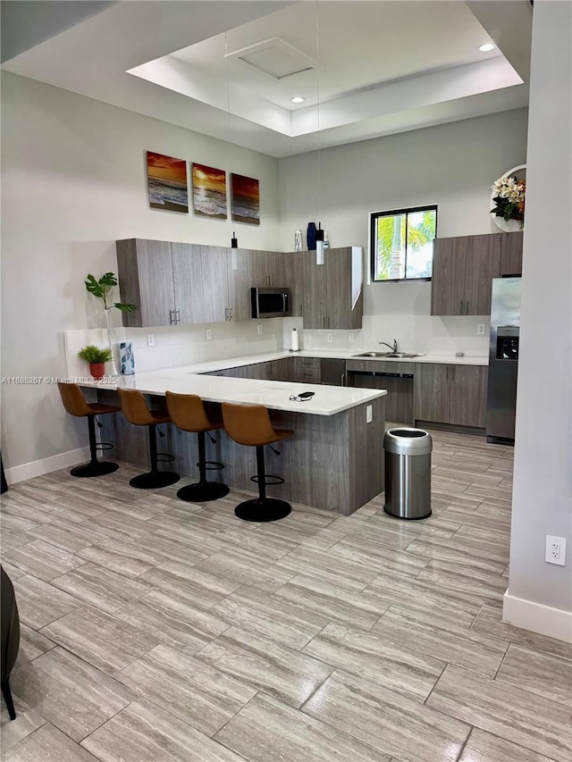 kitchen featuring sink, a raised ceiling, kitchen peninsula, a kitchen bar, and appliances with stainless steel finishes