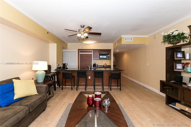 living room featuring sink, crown molding, light hardwood / wood-style flooring, and ceiling fan