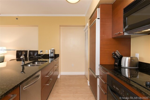 kitchen featuring sink, dark stone countertops, ornamental molding, light hardwood / wood-style floors, and black appliances