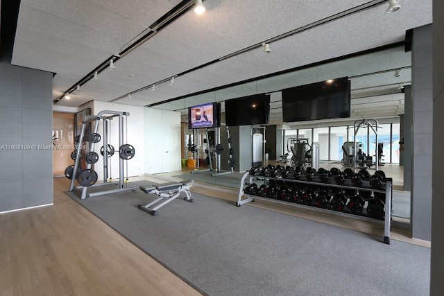 workout area with wood-type flooring, track lighting, and a textured ceiling