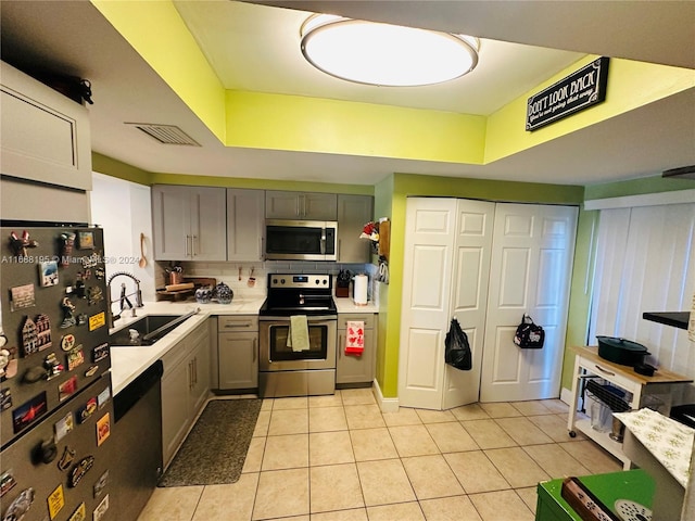 kitchen with sink, tasteful backsplash, gray cabinetry, light tile patterned flooring, and appliances with stainless steel finishes