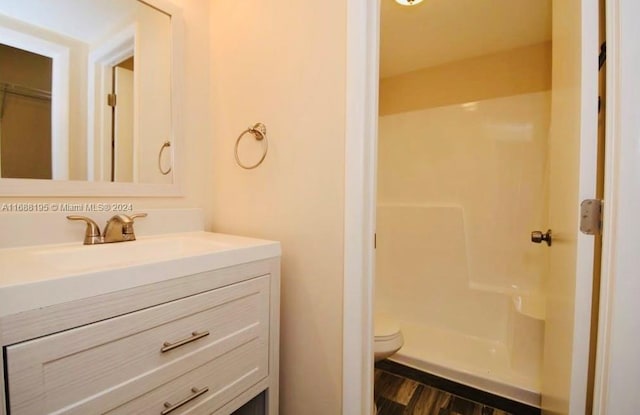 bathroom with toilet, a shower, vanity, and wood-type flooring