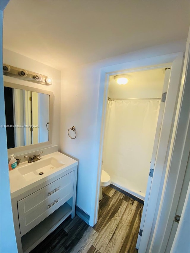 bathroom featuring wood-type flooring, walk in shower, vanity, and toilet