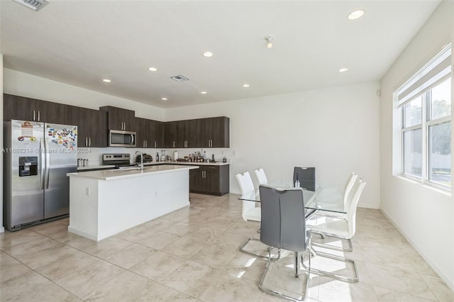 kitchen with dark brown cabinets, stainless steel appliances, and a center island with sink