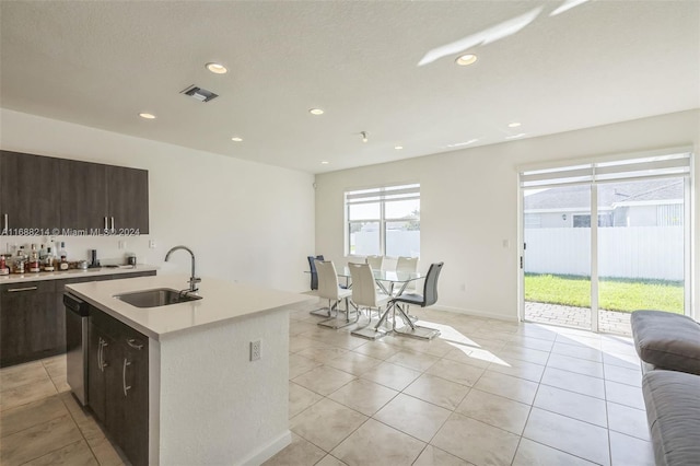 kitchen with a center island with sink, dark brown cabinetry, sink, light tile patterned floors, and stainless steel dishwasher