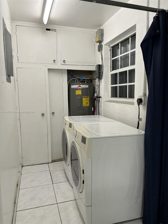 laundry area with electric water heater, washer and clothes dryer, light tile patterned floors, and cabinets