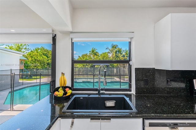 kitchen featuring sink, dishwasher, white cabinetry, backsplash, and dark stone counters