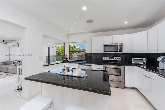 kitchen with white cabinetry, a wall mounted air conditioner, stainless steel appliances, and dark stone countertops