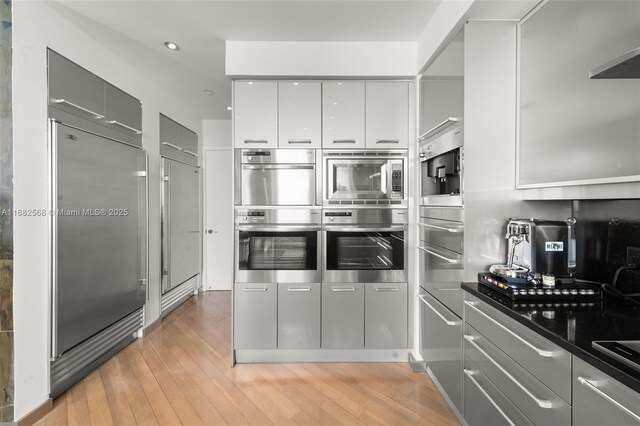 kitchen featuring gray cabinetry, stainless steel appliances, exhaust hood, and light hardwood / wood-style flooring