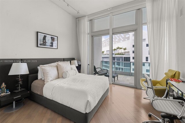 bedroom featuring wood-type flooring, access to exterior, a wall of windows, and track lighting