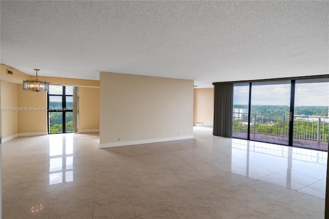 tiled empty room with a wealth of natural light, a textured ceiling, and a notable chandelier