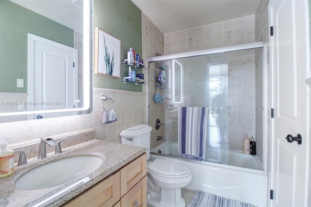 full bathroom featuring toilet, tile walls, tile patterned flooring, combined bath / shower with glass door, and vanity