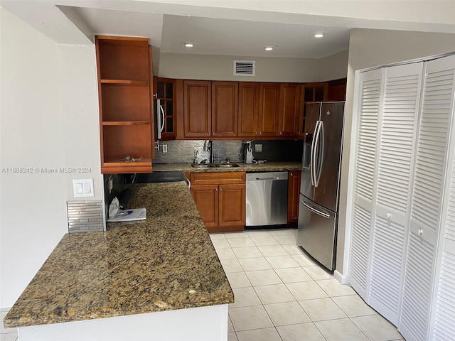 kitchen featuring backsplash, dark stone counters, sink, light tile patterned floors, and stainless steel appliances